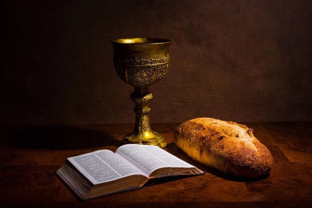A chalice and a loaf of bread beside an open Bible