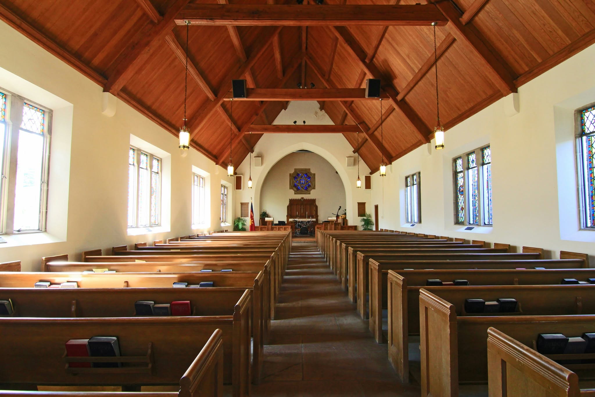 A church sanctuary of wooden pews under an open timber roof, stained glass down both walls